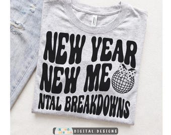 May include: A heather grey t-shirt featuring black text that reads NEW YEAR NEW ME NTAL BREAKDOWNS in a wavy font. A black and white disco ball with a polka dot bow is positioned to the right of the text. The shirt has a crew neckline and a tag.