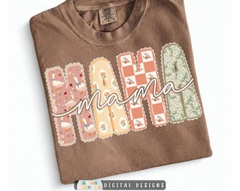 May include: A brown short-sleeve t-shirt featuring the word MAMA in large, scalloped-edge block letters. Each letter has a unique pattern: white geese on pink, yellow flowers, a peach checkerboard, and white daisies on green. The word mama is written in white cursive script across the center.
