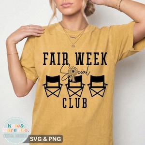 May include: A mustard yellow short-sleeve t-shirt featuring black text that reads FAIR WEEK SOCIAL CLUB. The design includes a graphic of three folding chairs and a ribbon award icon centered between the words Fair Week and Social.