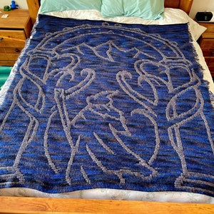 May include: A blue and gray crocheted blanket with a design of trees and mountains. The blanket is on a bed with two pillows.