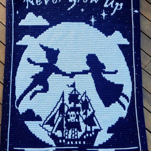 May include: A navy and light blue crochet blanket depicting a scene from Peter Pan. The design shows Peter Pan and Wendy flying in front of a moon, a pirate ship, and the words "Never Grow Up".