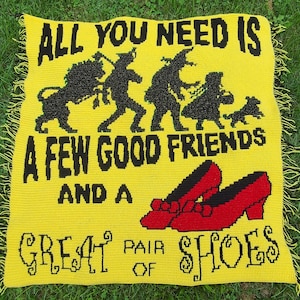 May include: Yellow crocheted blanket with the text "All you need is a few good friends and a great pair of shoes". The blanket features black silhouettes of characters from the Wizard of Oz.