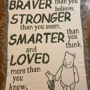 May include: A white crocheted blanket with green text that reads "Always remember, you are BRAVER than you believe, STRONGER than you seem, SMARTER than you think, and LOVED more than you know." The blanket features a green and white crocheted image of Winnie the Pooh and Piglet.