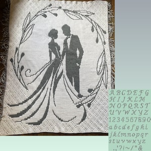 May include: A white crocheted blanket with a gray silhouette of a bride and groom standing in a wreath of leaves. The blanket has a fringe border.