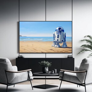 May include: A white and blue robot stands on a sandy beach with a blue ocean and sky in the background. The robot is facing away from the viewer and has a round head with a single eye.