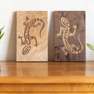 Peut inclure: Deux décorations murales en bois représentant un lézard stylisé. Le lézard est sculpté dans le bois et est de couleur brun clair. Le bois est de couleur brun clair avec un motif de grain naturel. Le bois à droite est de couleur brun foncé.