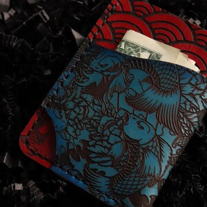 May include: A blue and red leather wallet with a Japanese-inspired design. The wallet has a flap that folds over and a pocket on the inside. The wallet is made of high-quality leather and has a unique design.