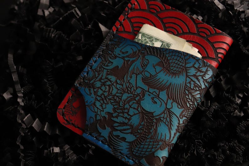 May include: A blue and red leather wallet with a Japanese-inspired design. The wallet has a flap that folds over and a pocket on the inside. The wallet is made of high-quality leather and has a unique design.