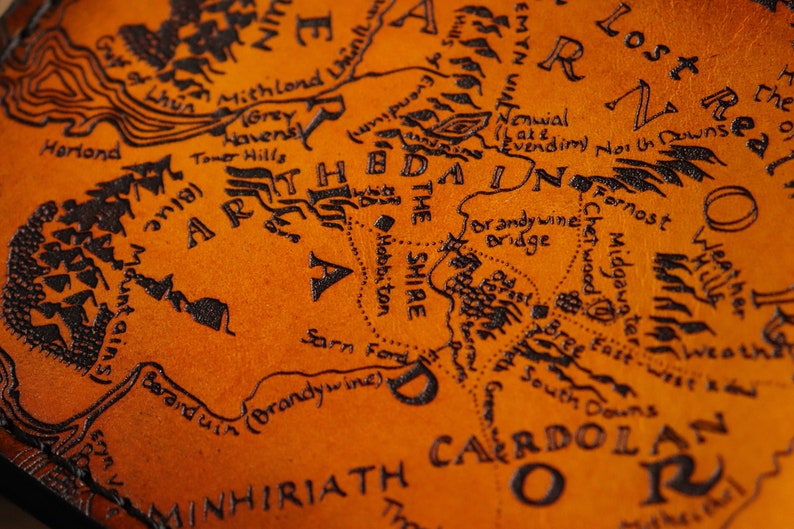 May include: A close-up of a leather map of Middle-earth from The Lord of the Rings. The map is brown with black ink and features the Shire, the Brandy Wine River, and the surrounding areas.
