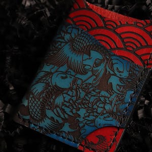 May include: A blue and red leather wallet with a koi fish and wave pattern. The wallet is embossed with a detailed design.