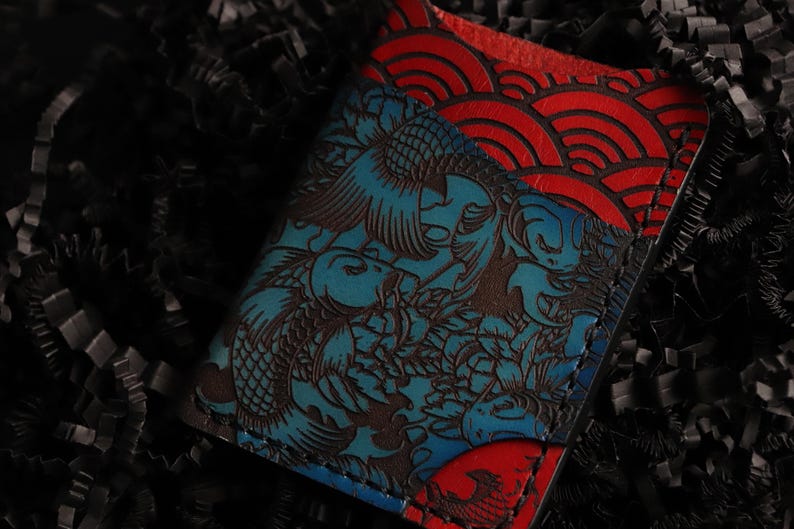 May include: A blue and red leather wallet with a koi fish and wave pattern. The wallet is embossed with a detailed design.