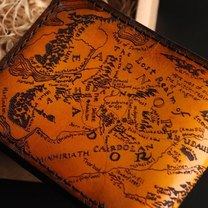 May include: A brown leather wallet with a map of Middle-earth from The Lord of the Rings engraved on the front. The map includes the Shire, Mordor, and the Misty Mountains.