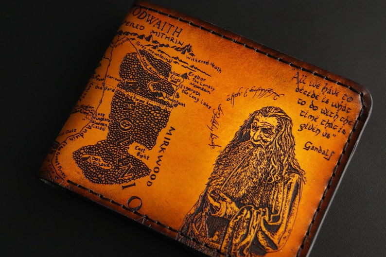 May include: A brown leather wallet with a map of Middle-earth and a portrait of Gandalf. The quote "All we have to decide is what to do with the time that is given us" is printed on the wallet.