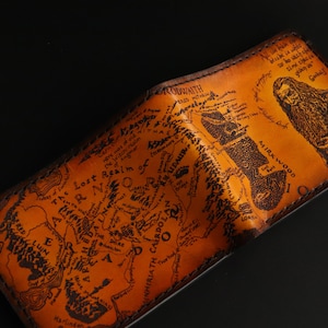 May include: A brown leather wallet with a map of Middle-earth from The Lord of the Rings printed on the front. The map includes the text "The Lost Realm of Mordor" and "Mirkwood".