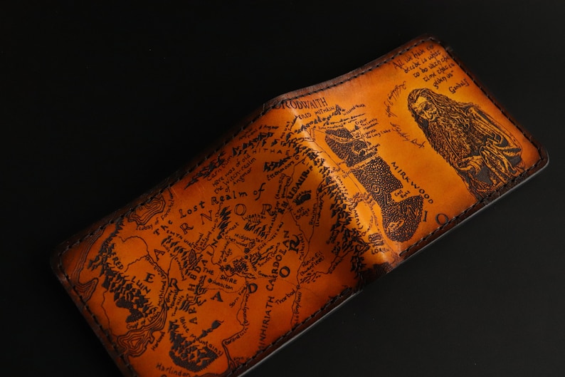 May include: A brown leather wallet with a map of Middle-earth from The Lord of the Rings printed on the front. The map includes the text "The Lost Realm of Mordor" and "Mirkwood".