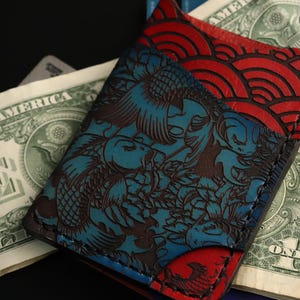 May include: A blue and red leather wallet with a koi fish and wave pattern. The wallet is made of high-quality leather and has a unique design.