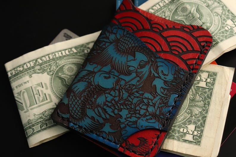 May include: A blue and red leather wallet with a koi fish and wave pattern. The wallet is made of high-quality leather and has a unique design.