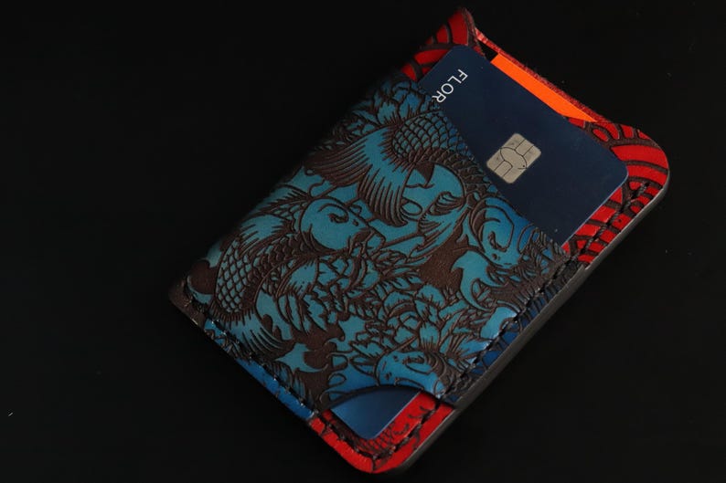 May include: A blue and red leather wallet with a koi fish design. The wallet has a slot for cards and a flap that closes with a snap.