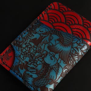 May include: A blue and red leather wallet with a Japanese-inspired design. One side features a blue background with a brown floral pattern and the other side features a red background with a wave pattern.