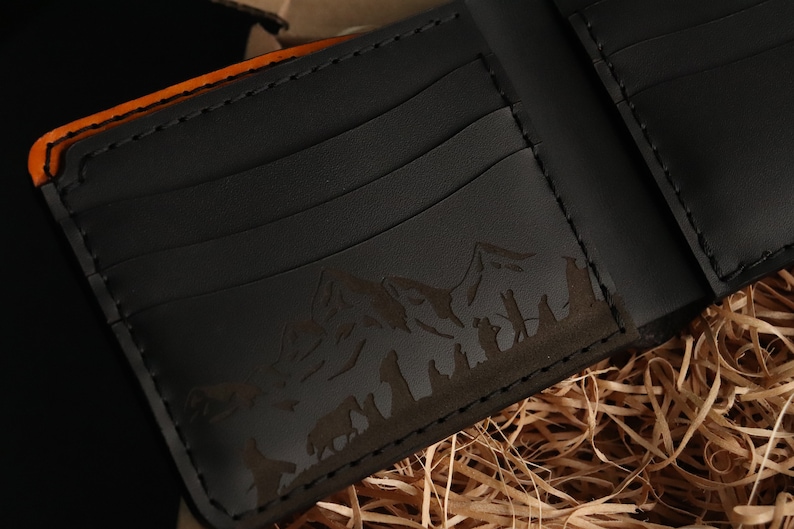 May include: A black leather wallet with an orange edge and an embossed mountain scene. The wallet has multiple card slots.