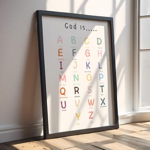 Puede incluir: Una impresión enmarcada con las palabras "God is...." en la parte superior. La impresión presenta el alfabeto con una palabra que comienza con cada letra. Las letras son de varios colores y el marco es negro.