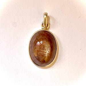 Peut inclure: Un pendentif doré avec une pierre précieuse ovale et brune. La pierre précieuse a un aspect translucide avec des motifs internes. Le pendentif a un design simple et élégant, adapté au quotidien ou aux occasions spéciales.