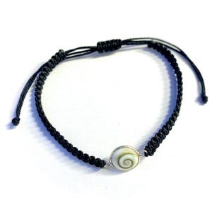 May include: A black braided cord bracelet with a white and brown shell charm.