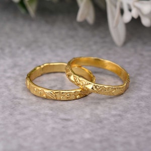 Puede incluir: Dos anillos de color dorado con intrincados diseños florales. Los anillos están apilados uno encima del otro.