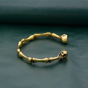 May include: A gold-toned bracelet with a skull design. The bracelet is made of a series of connected bone-shaped links.