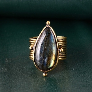 May include: A gold ring with a teardrop-shaped labradorite gemstone. The ring has a multi-layered band.