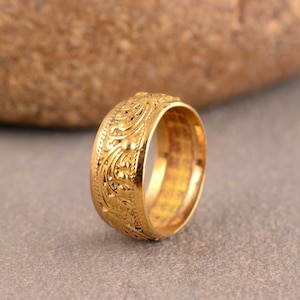 May include: A gold band ring with a detailed floral design. The ring is made of a smooth, polished metal and has a classic, elegant style.