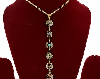 May include: A gold chain necklace with seven chakra symbols and gemstones. Each symbol is a mandala with a gemstone in the center. The gemstones are purple, blue, turquoise, green, yellow, orange, and red.