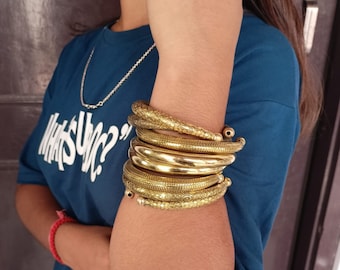 Puede incluir: Una pila de brazaletes de metal dorado con diseños intrincados. Los brazaletes se llevan en la muñeca.