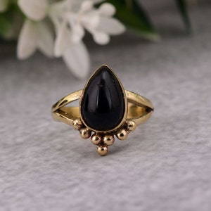 May include: A gold ring featuring a black teardrop-shaped gemstone. The ring has a delicate design with small beads surrounding the gemstone.