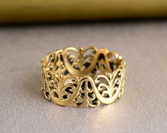 Puede incluir: Un anillo de filigrana dorado con un diseño delicado e intrincado. El anillo está hecho de un metal fino y tiene una banda ancha.