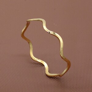 Op de afbeelding: Een golvende ring van goudkleurig metaal. De ring is gemaakt van één stuk metaal dat in een golvende vorm is gebogen.