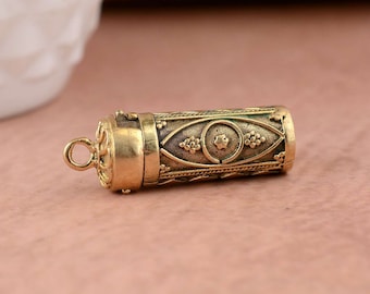May include: A gold-toned metal container with an intricate design. The container has a hinged lid and a small loop for attaching a chain.