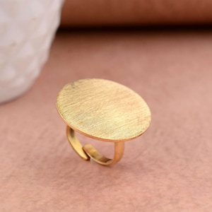 May include: A gold-toned ring with a large, round, flat top. The top of the ring has a brushed finish.