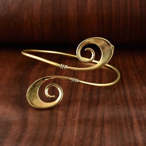 May include: A gold-toned metal bracelet with a swirling design. The bracelet is open and has a simple clasp.