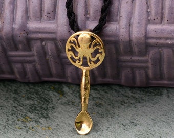 May include: A gold necklace with a pendant shaped like a spoon with an octopus design. The pendant is attached to a black cord.