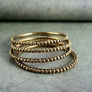 May include: Four gold-toned bangles with a beaded design. The bangles are stacked on top of each other.