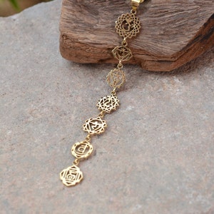 May include: A gold necklace with seven chakra symbols, including Om, hanging from a chain. The necklace is displayed on a wooden surface.