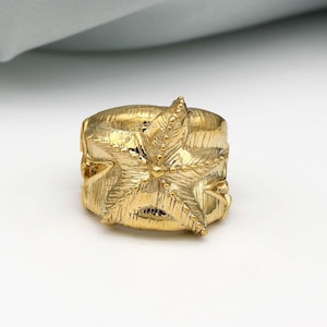 May include: A gold-toned ring featuring a detailed starfish design. The ring is made of metal and has a textured finish.
