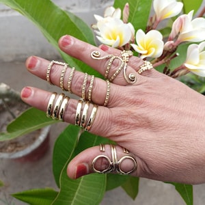 Könnte beinhalten: Eine Hand trägt einen Satz goldfarbener Ringe, darunter ein einzigartiger Spiralring und mehrere übereinanderliegende Ringe.