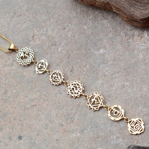May include: A gold necklace with seven chakra symbols, including the Om symbol, hanging from a delicate chain.