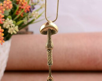 May include: A gold-toned necklace with a mushroom-shaped pendant. The pendant is detailed with a stem and a spoon at the bottom.