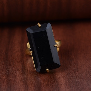 Puede incluir: Un anillo de oro con una gran piedra rectangular negra.