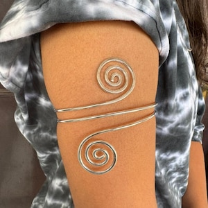 Puede incluir: Brazalete de brazo plateado con dos diseños en espiral. El brazalete está hecho de metal delgado y es ajustable.