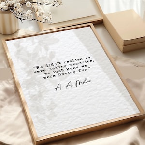 May include: A framed print with a gold-colored frame. The print features the quote, "We didn't realise we were making memories, we just knew we were having fun." by A. A. Milne, in black text on a white background.