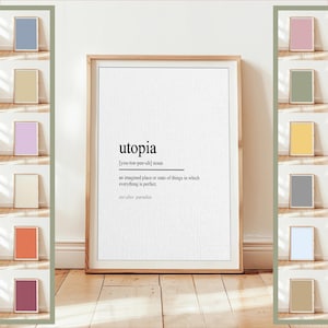 Puede incluir: Una impresión enmarcada con la definición de "utopía" en texto negro sobre un fondo blanco. El marco es de color marrón claro y la impresión se muestra sobre un suelo de madera. Se ven impresiones enmarcadas adicionales en varios colores.